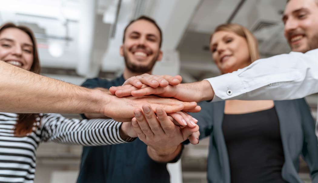 4 Junge Menschen legen hände aufeinander und visualisieren teamwork/ teamgeist.